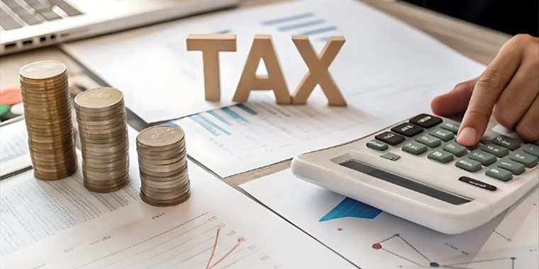 Letras de madeira formando a palavra TAX sobre mesa com calculadora e moedas